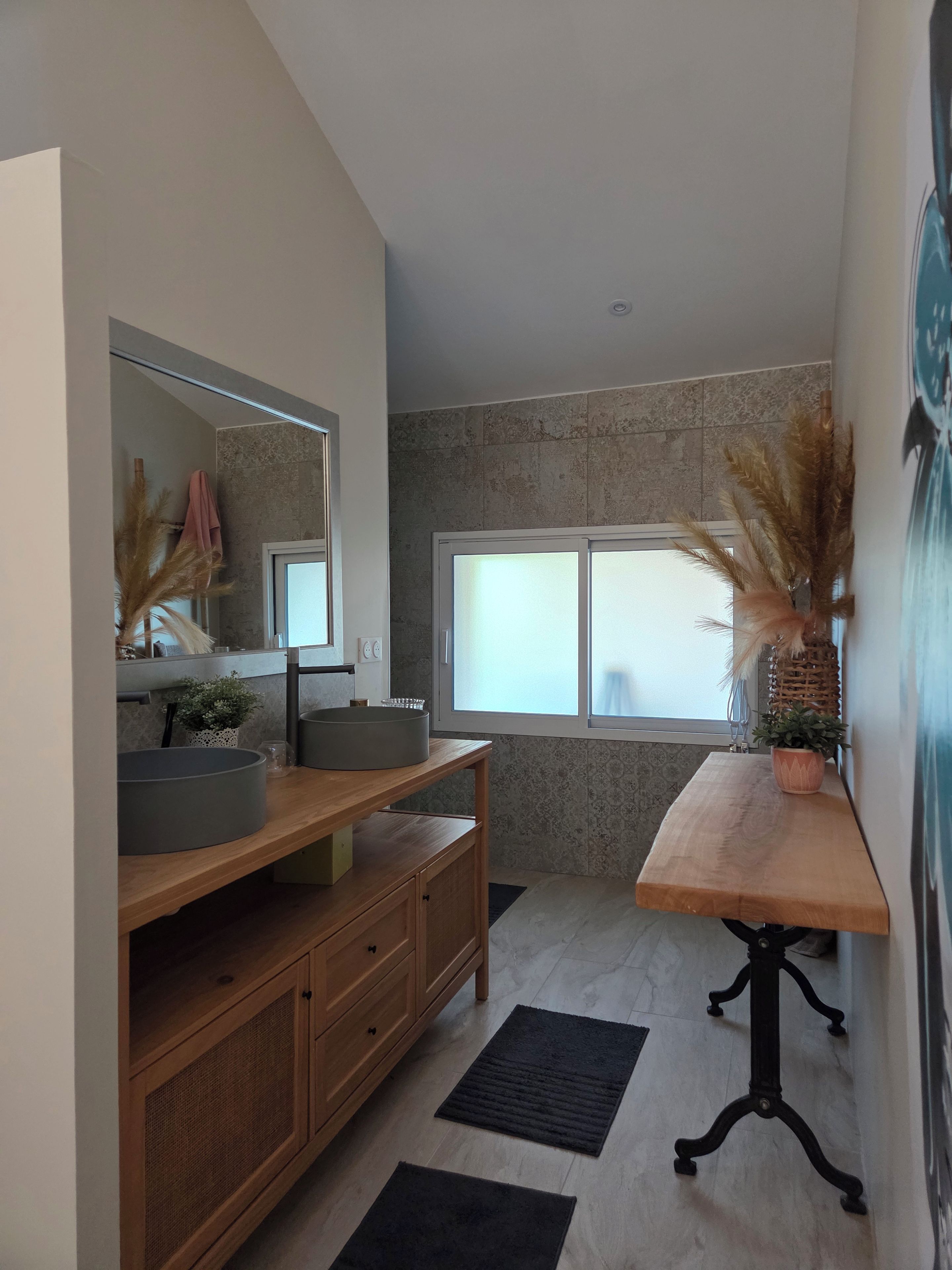 A modern bathroom with a large mirror, a wooden vanity, a round sink, and a window with a view.