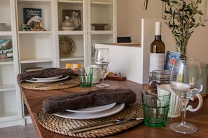 A dining table set with plates, cutlery, glasses, and a bottle of wine, with a bookshelf in the background. - Farm Lodges Olive, Casa Jacaranda, Moncarapacho Countryside (Moncarapacho)