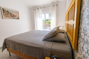 A bedroom with a bed, a window with curtains, a wooden headboard, and a painting on the wall. - Farm Lodges Olive, Casa Jacaranda, Moncarapacho Countryside (Moncarapacho)