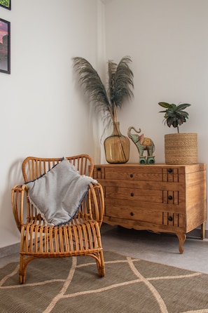 A wicker chair with a throw blanket, a wooden cabinet with decorative items, and a patterned rug. - Farm Lodges Olive, Casa Jacaranda, Moncarapacho Countryside (Moncarapacho)