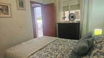 Un dormitorio con cama, cómoda, ventilador y ventana con cortinas.