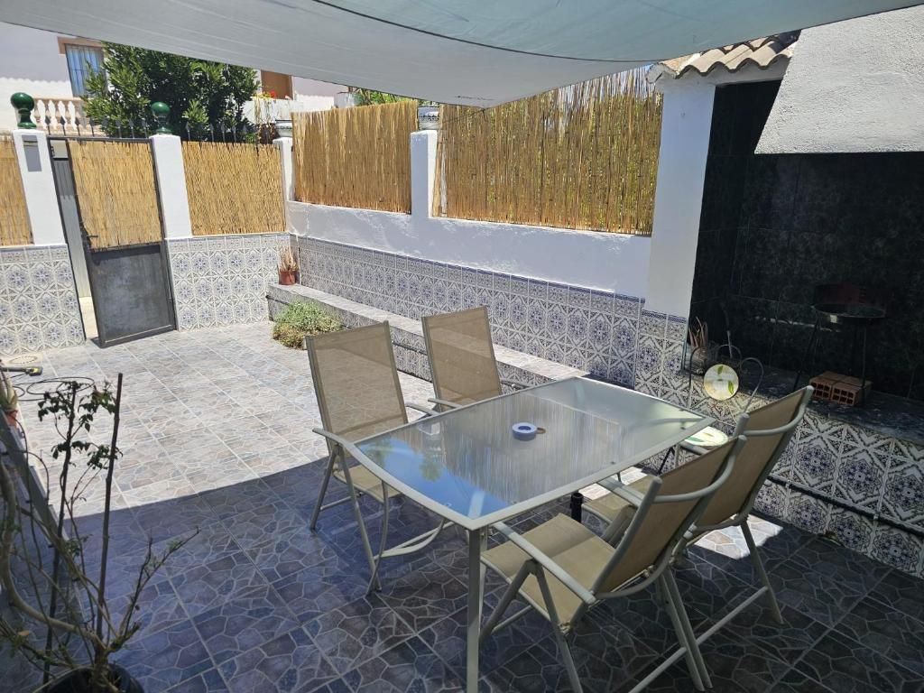 An outdoor patio with a glass table and chairs, a barbecue grill, and a tiled floor.