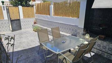 An outdoor patio with a glass table and chairs, a barbecue grill, and a tiled floor.