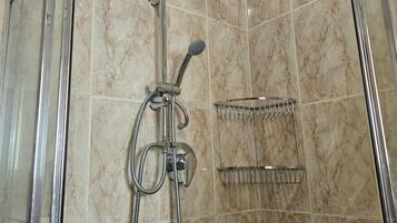 Aseo con ducha empotrada, cabezal de ducha de mano y tipo lluvia, puerta de vidrio y toallero metálico.