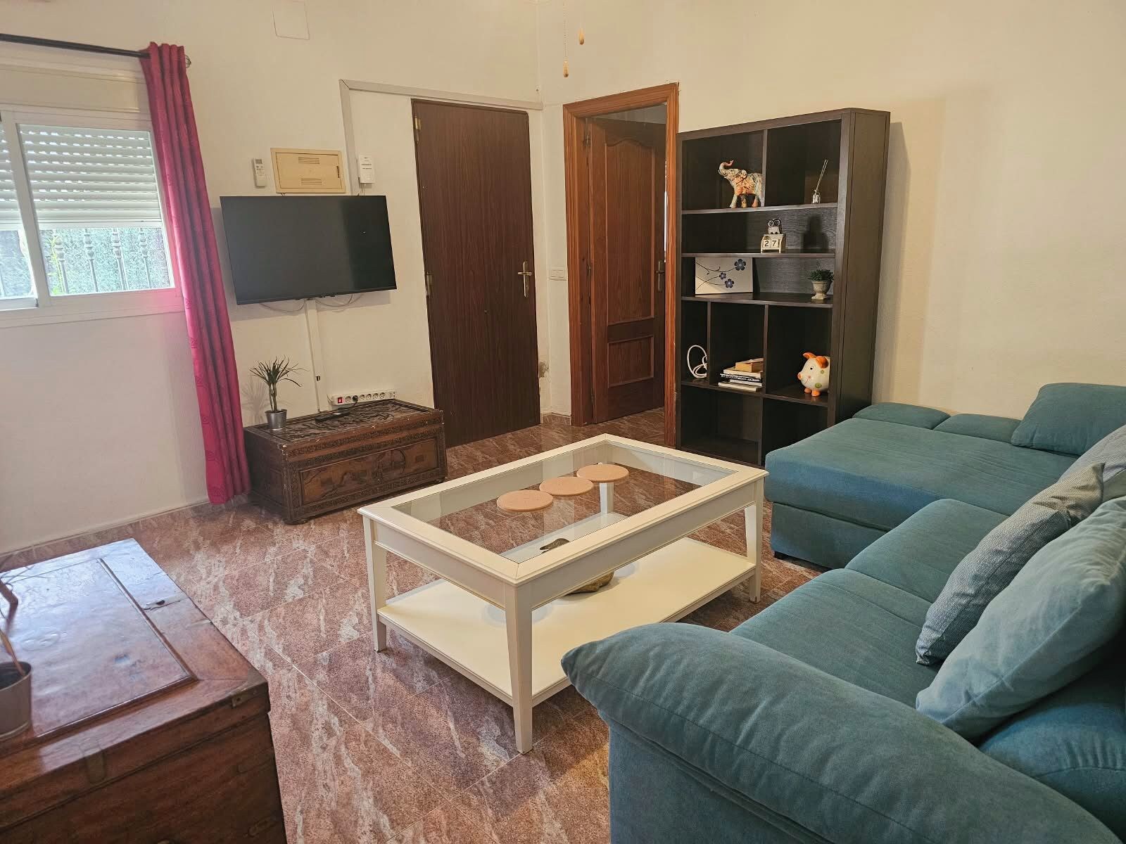 Una sala de estar con un sofá, una mesa de centro, una televisión y una estantería.