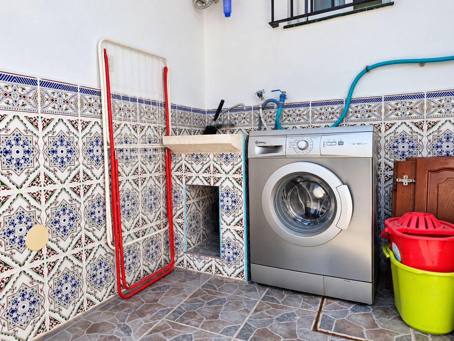 Een kleine wasruimte met een wasmachine, een droogrek en een betegelde spatwand.