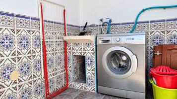 Een kleine wasruimte met een wasmachine, een droogrek en een betegelde spatwand.