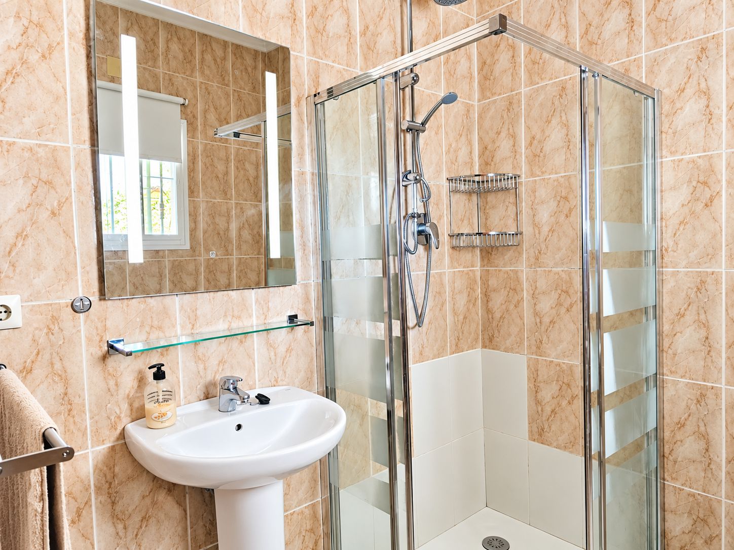 Un baño con ducha envuelta en vidrio, un lavamanos blanco y un espejo sobre él.