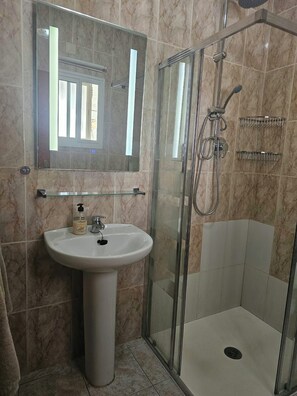 Un bagno con cabina doccia in vetro, lavabo su piedistallo e specchio sopra il lavabo.