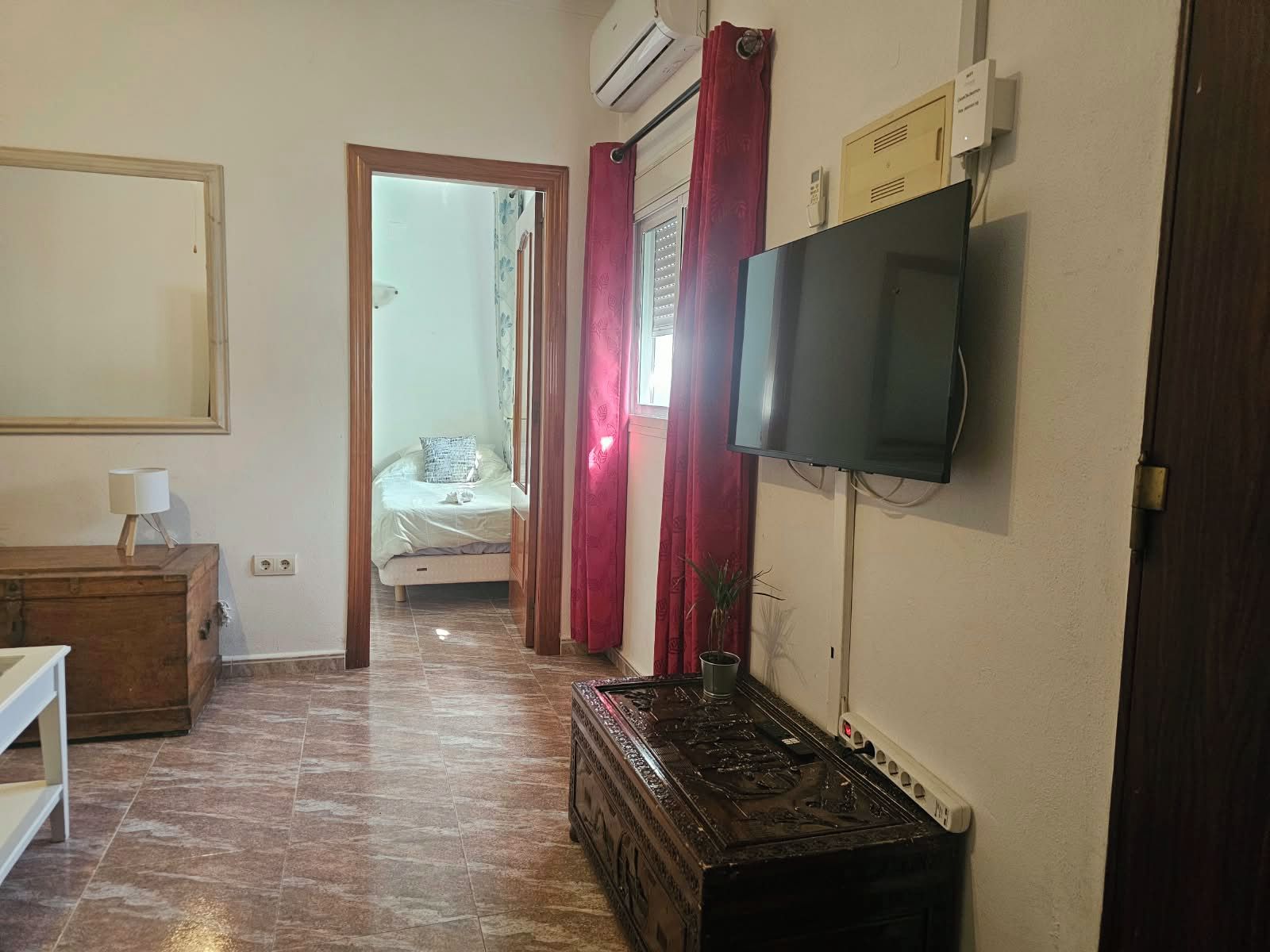 Una habitación de hotel con una cama, un televisor montado en la pared, un aparador de madera y piso de baldosas.