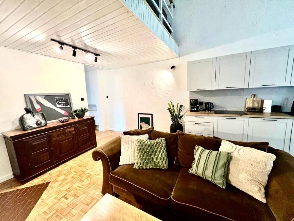 Uma sala de estar com sofá marrom, mesa de centro de madeira e área de cozinha com armários brancos e bancada.