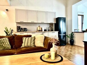 Una sala moderna con un sofá de cuero marrón, una mesa de centro de madera y una cocina con gabinetes blancos y un refrigerador negro.