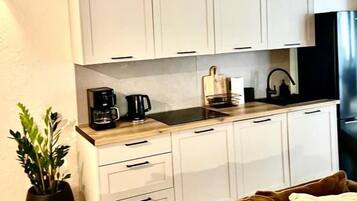 A compact kitchen with white cabinets, a coffee maker, and a black refrigerator.