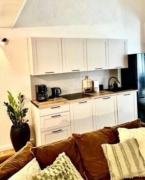A compact kitchen with white cabinets, a coffee maker, and a black refrigerator.