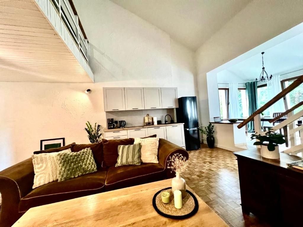 A modern living space with a wooden dining table, a brown sofa, and a kitchen area with white cabinets.