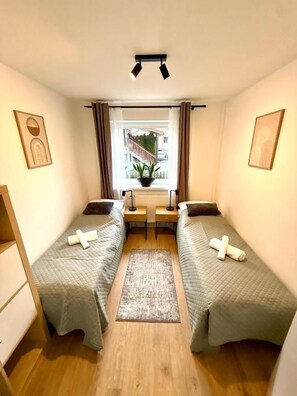 Una habitación pequeña con dos camas, una ventana con cortinas, un escritorio y una planta en maceta.