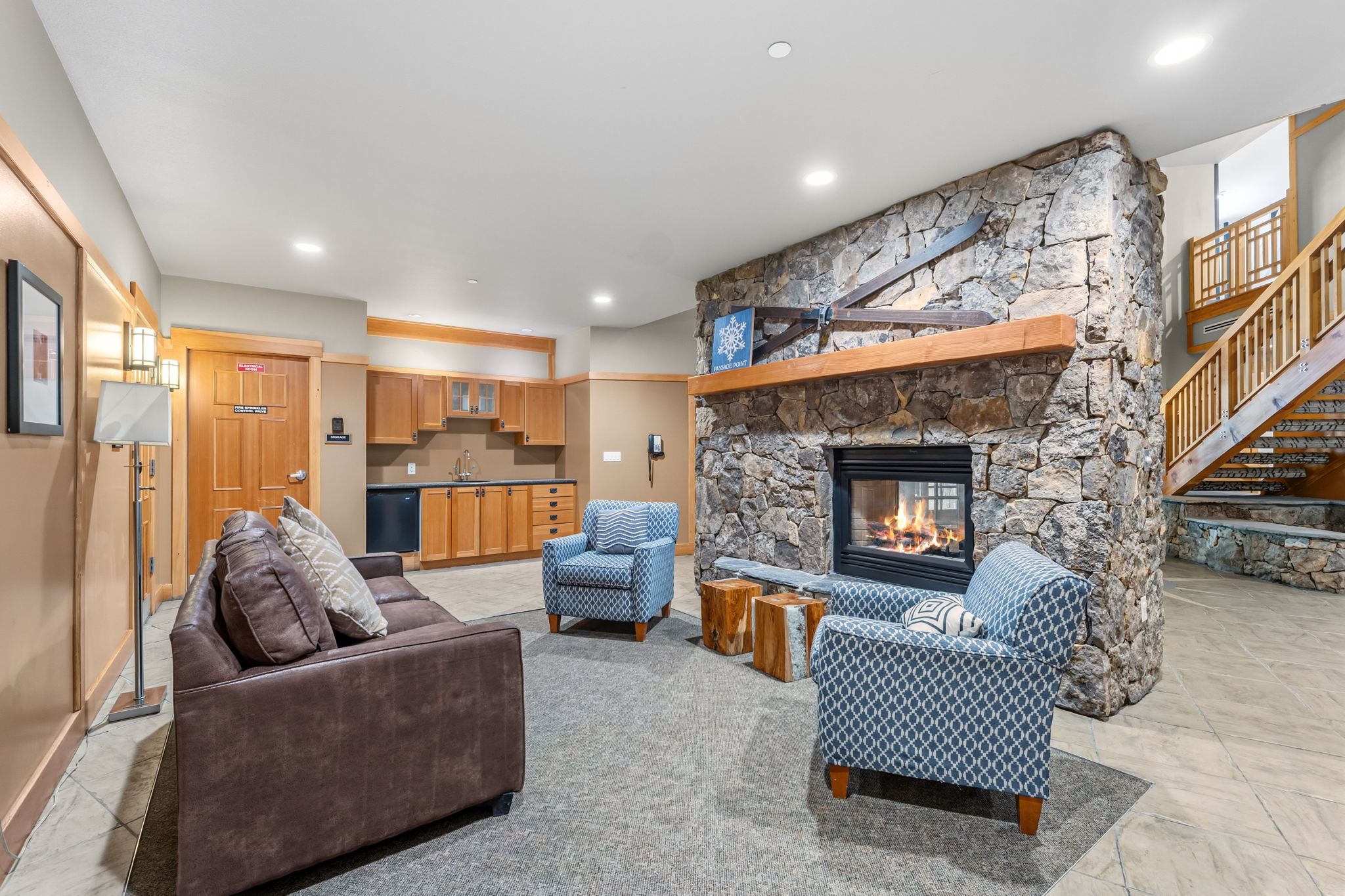 A spacious living area with a stone fireplace, a kitchen in the background, and a staircase leading to an upper level.