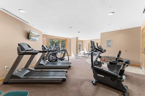 Ett gym med löpband, motionscyklar och en TV som är monterad på väggen.