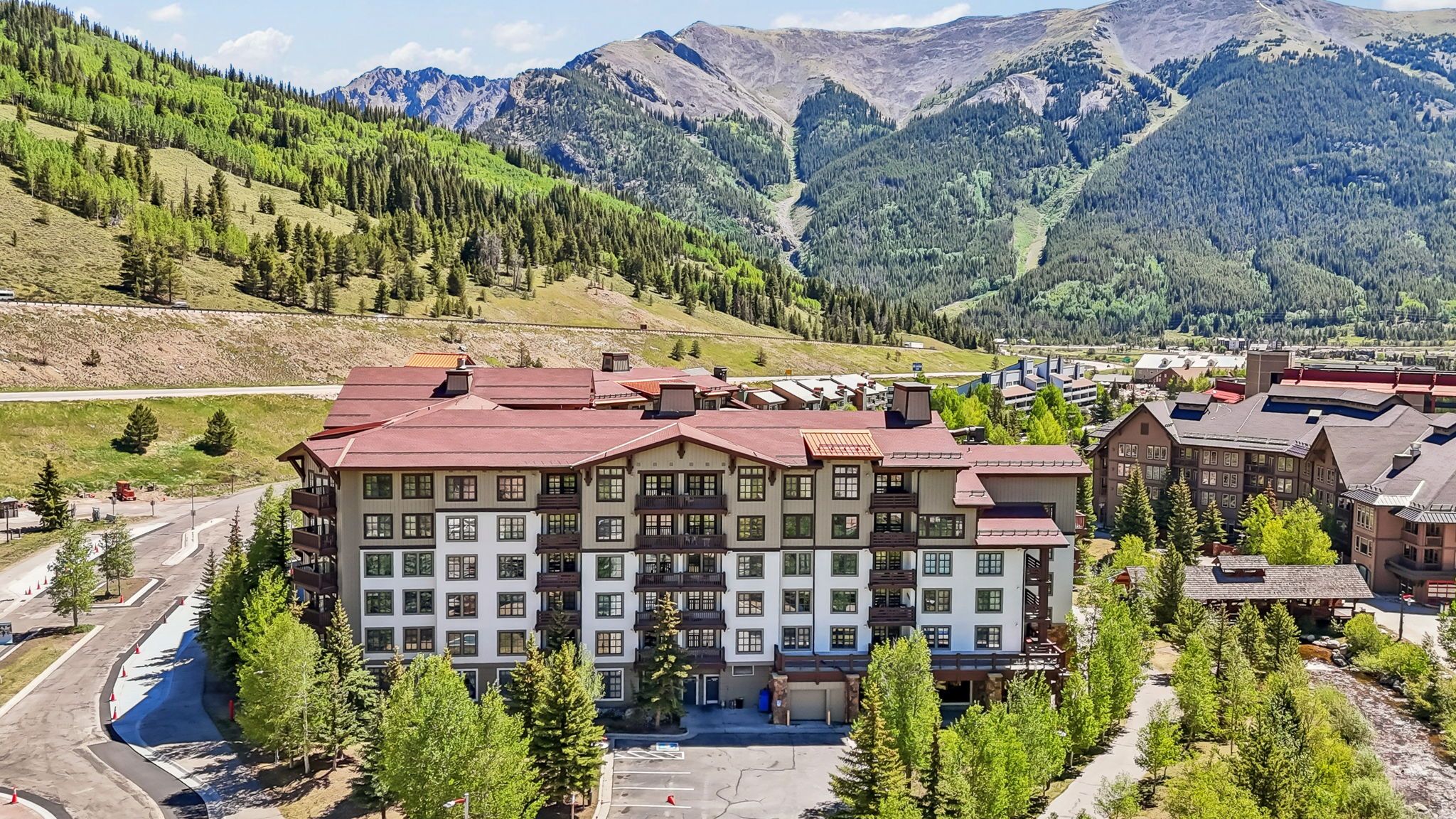 Ein mehrstöckiges Hotel mit rotem Dach, umgeben von Grünflächen und Bergen.