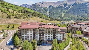 Ein mehrstöckiges Hotel mit rotem Dach, umgeben von Grünflächen und Bergen.