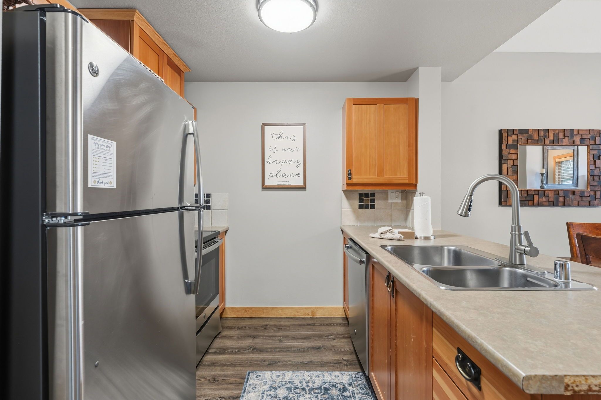 A modern kitchen with stainless steel appliances, wooden cabinets, a double sink, and a decorative wall piece.
