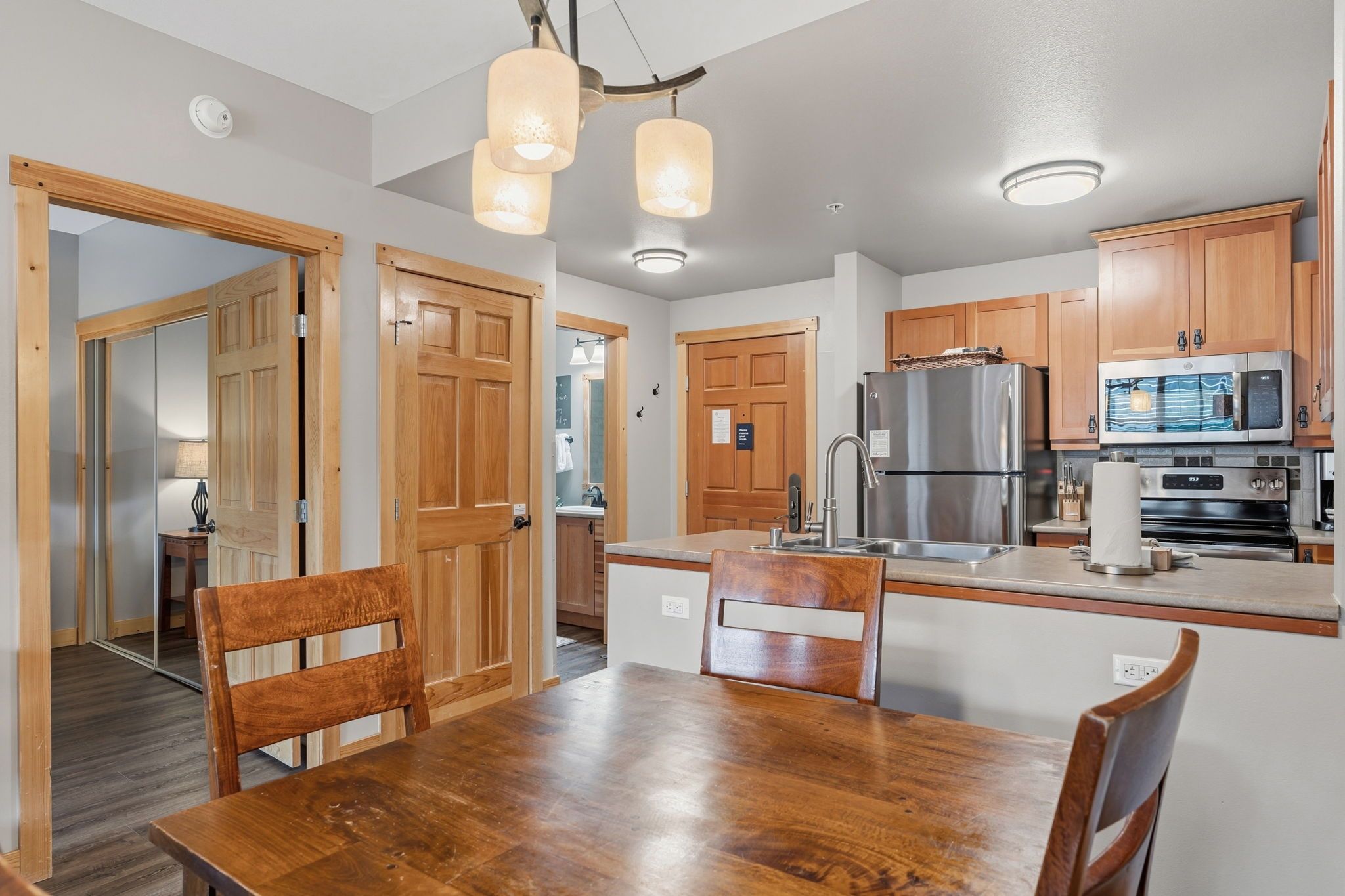 A modern kitchen with wooden cabinets, stainless steel appliances, and a dining area with a wooden table and chairs.