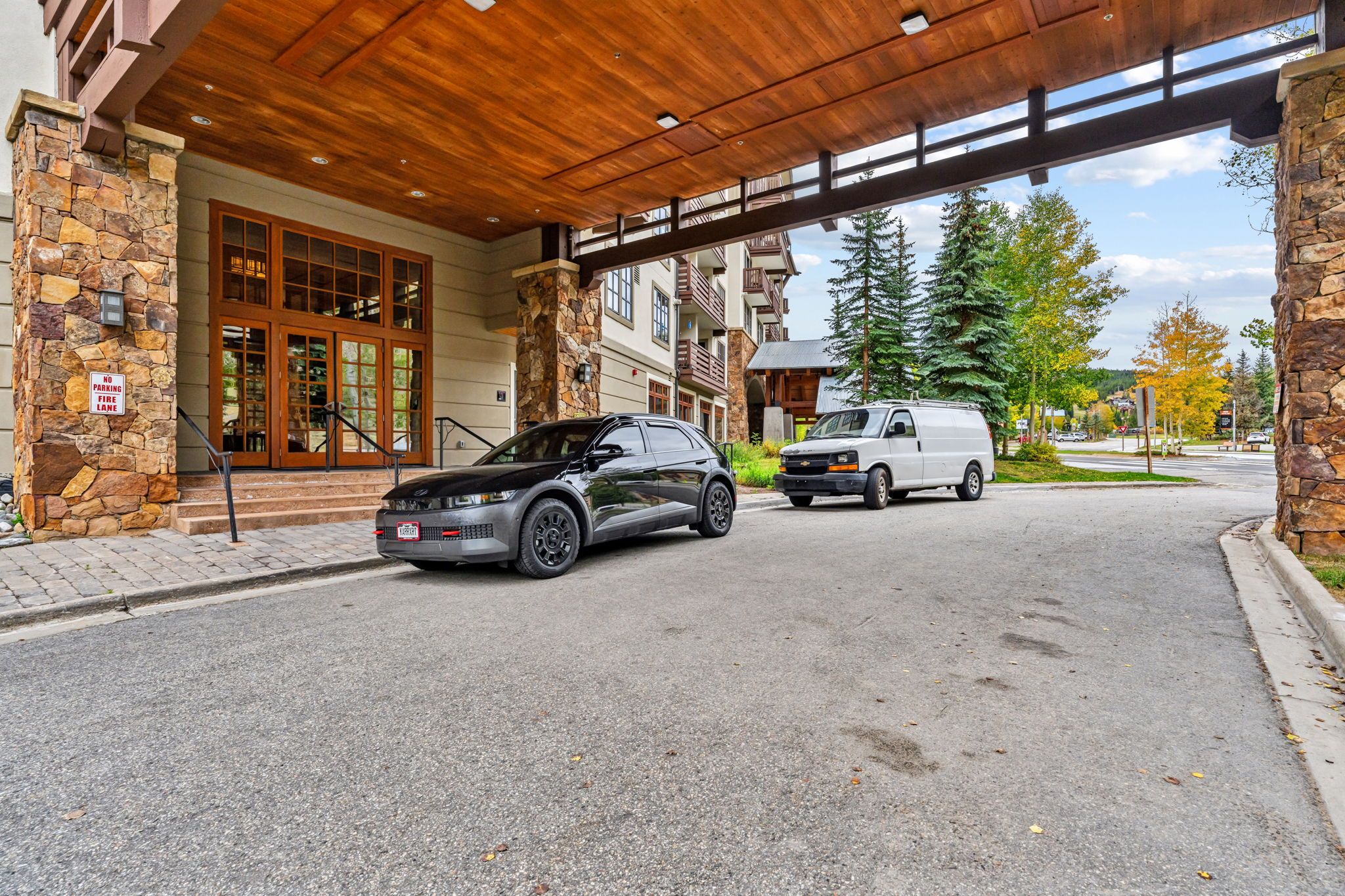 A building entrance with a stone facade, a covered walkway, and a parked car and van.