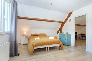 Une chambre avec un plafond en pente, un lit avec une serviette roulée, une table de chevet avec une lampe, une commode et une fenêtre avec des rideaux.