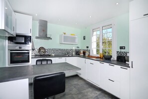 A modern kitchen with white cabinets, a black countertop, and a window with a view of trees. - Loargann ker Pondi - Maison pour 6 (Pontivy)