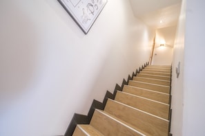 Eine Treppe mit Holzsitzen und schwarzen Kanten, die zu einer Zwischenebene mit einer Leuchte führt.