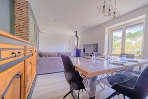 A modern interior with a dining area, kitchen, and a large window. - La Maison des Salines - Proche de la Gare (Varangéville)