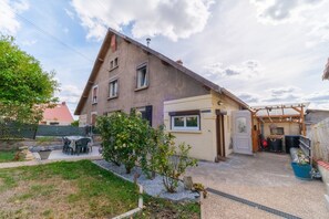 A two-story house with a sloped roof, a front porch, and a small garden area with a table and chairs. - La Maison des Salines - Proche de la Gare (Varangéville)