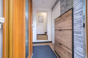 A hallway with a wooden door, a wall-mounted picture, a staircase, and a wardrobe with a herringbone pattern. - La Maison des Salines - Proche de la Gare (Varangéville)