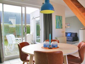 A dining area with a round table, chairs, a blue pendant light, and a view through a glass door to an outdoor patio. - Holiday Apartment With 2 Bedrooms (Callantsoog)