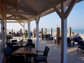 Ein Sitzbereich im Freien mit Tischen und Stühlen mit Blick auf einen Strand.