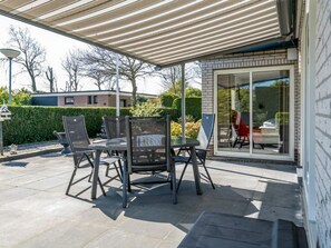 Eine Terrasse im Freien mit Tisch und Stühlen, einem überdachten Bereich und einer Glasdoor, die zu einem Raum führt.