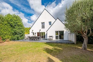 A white two-story house with a patio, a dining area, and a large tree in the foreground. - Ker-eole - A côté du Port de la Trinité (La Trinite-sur-Mer)