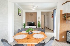 A modern dining area with a wooden table, grey upholstered chairs, a television, and a ceiling fan. - Au haut de Lolo - Piscine Privée (Morne-A-l'Eau)