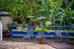 Eine Terrasse mit Steinboden, zwei blauen Stühlen, einem Blumentopf und einem blauen Zaun.