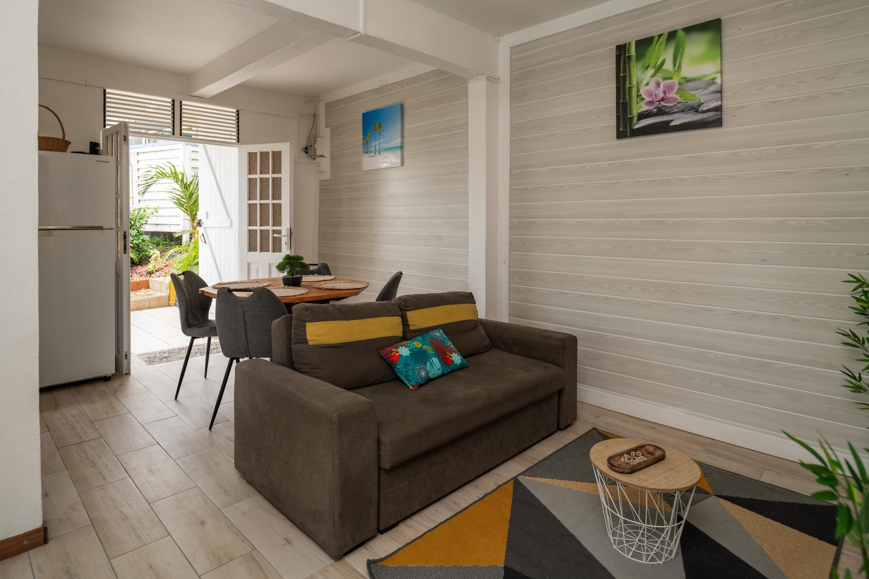 Un salon moderne comprenant un canapé, une table à manger avec des chaises, un coin cuisine et une vue sur l’extérieur.