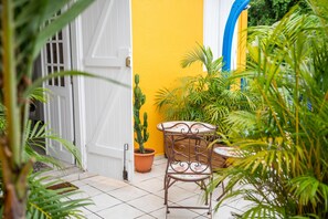 A small patio area with a white door, a yellow wall, and a potted cactus. There is a metal chair and a small table with a mosaic top. - Au haut de Lolo - Piscine Privée (Morne-A-l'Eau)