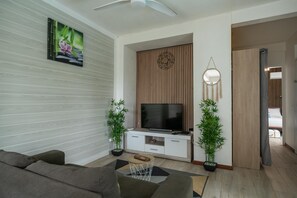 Ein modernes Wohnzimmer mit Flachbildfernseher, einer Couch, einem Couchtisch und zwei Blumentöpfen.