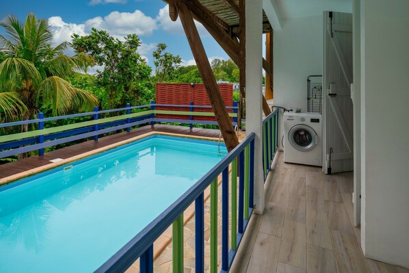 Ein Schwimmbecken mit einer Holzterrasse und einer Waschmaschine im Hintergrund.