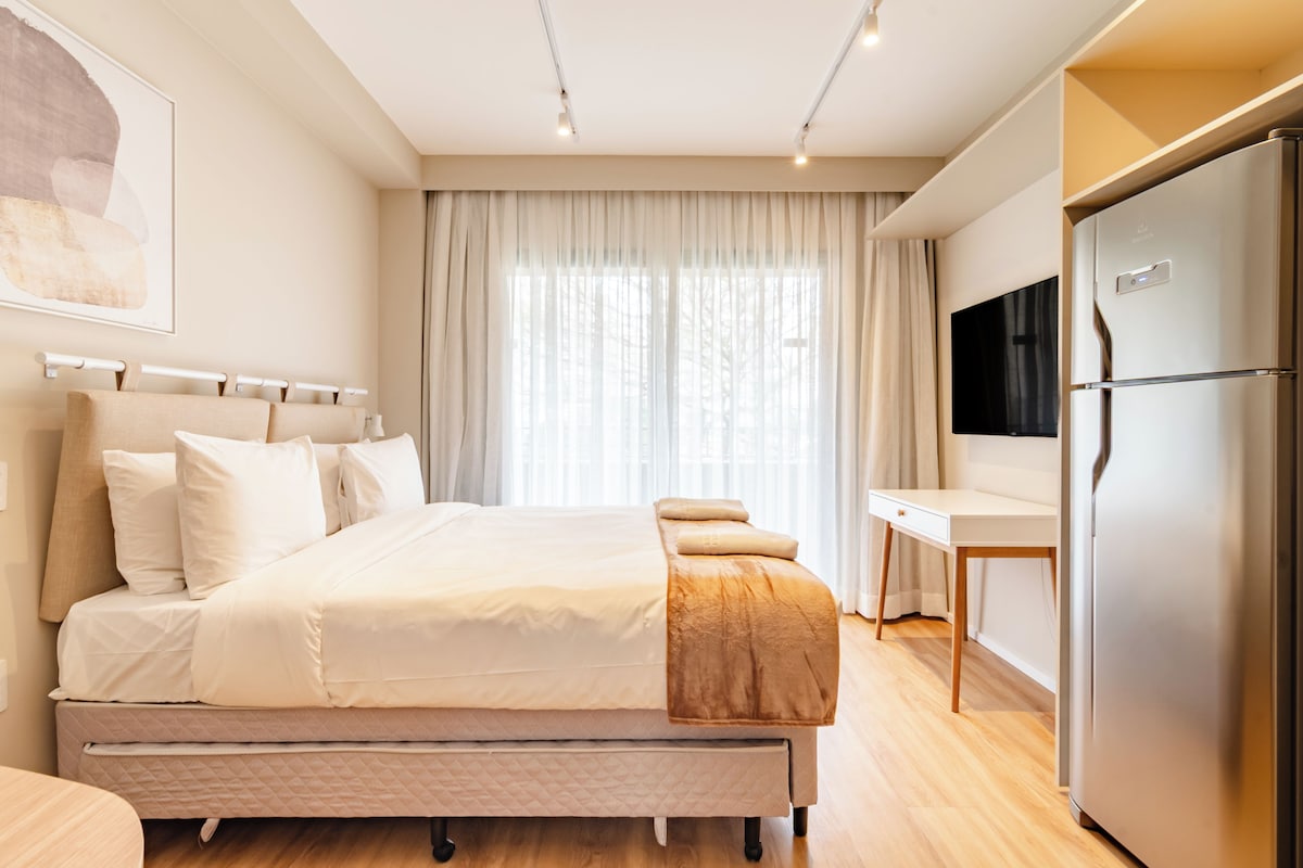 A modern bedroom with a bed, a desk, and a refrigerator.
