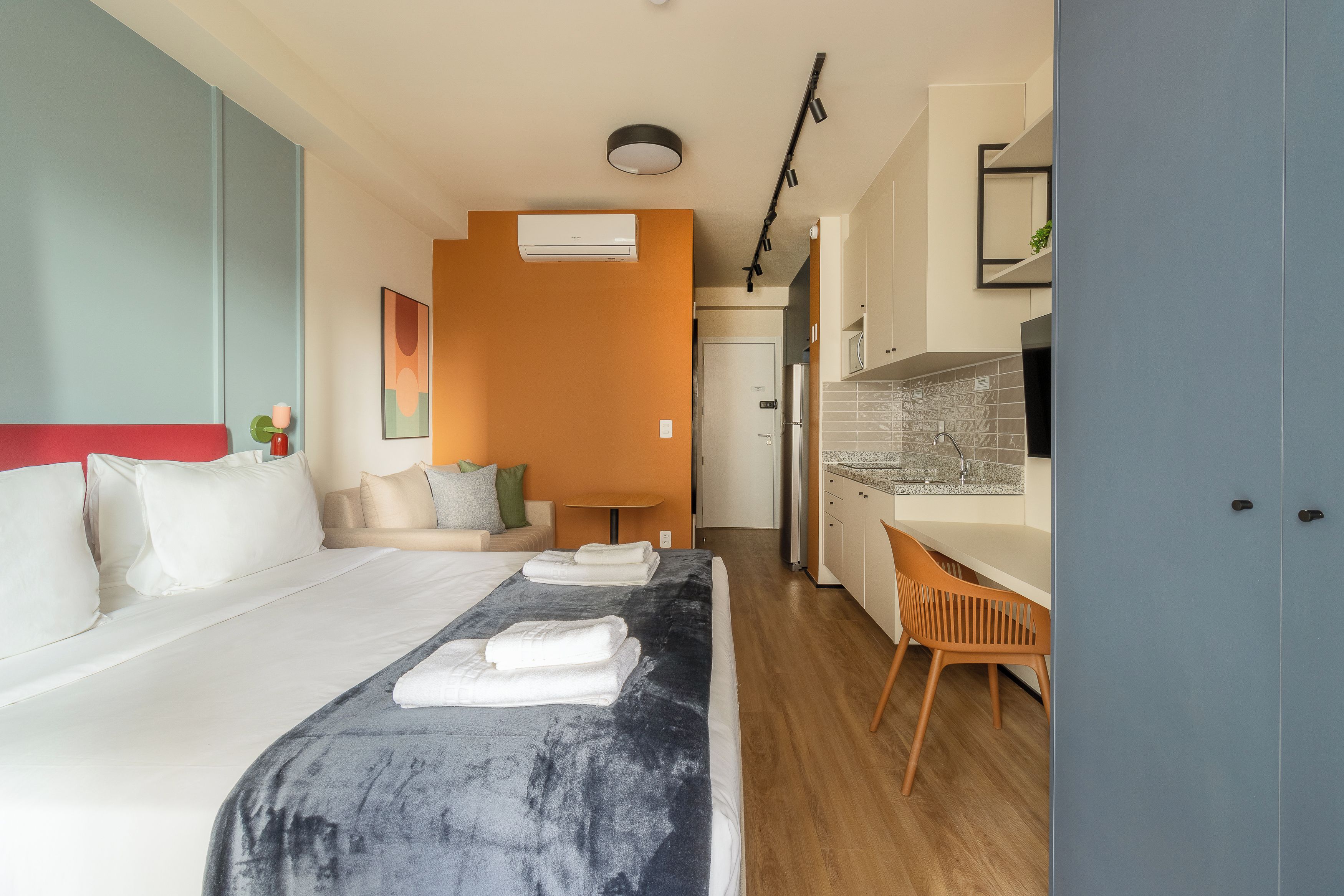 Ett hotellrum med en säng, ett skrivbord, en stol, ett litet kök och ett badrum.