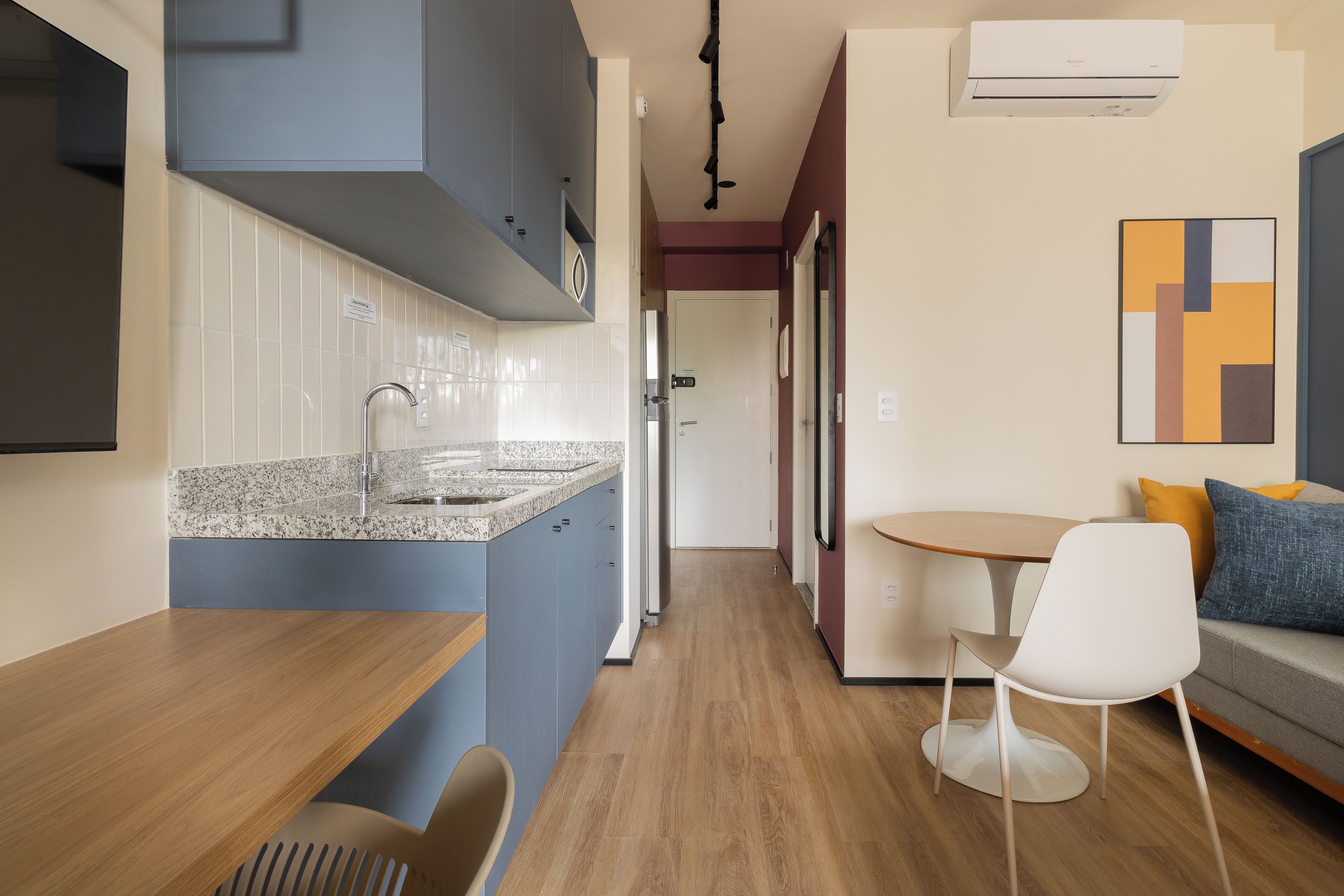 A modern kitchen with a granite countertop, a built-in sink, and a stainless steel refrigerator. There is a dining area with a wooden table and a white chair.