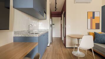 A modern kitchen with a granite countertop, a built-in sink, and a stainless steel refrigerator. There is a dining area with a wooden table and a white chair.