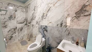 A bathroom with a toilet, sink, and shower area, featuring marble tiles.