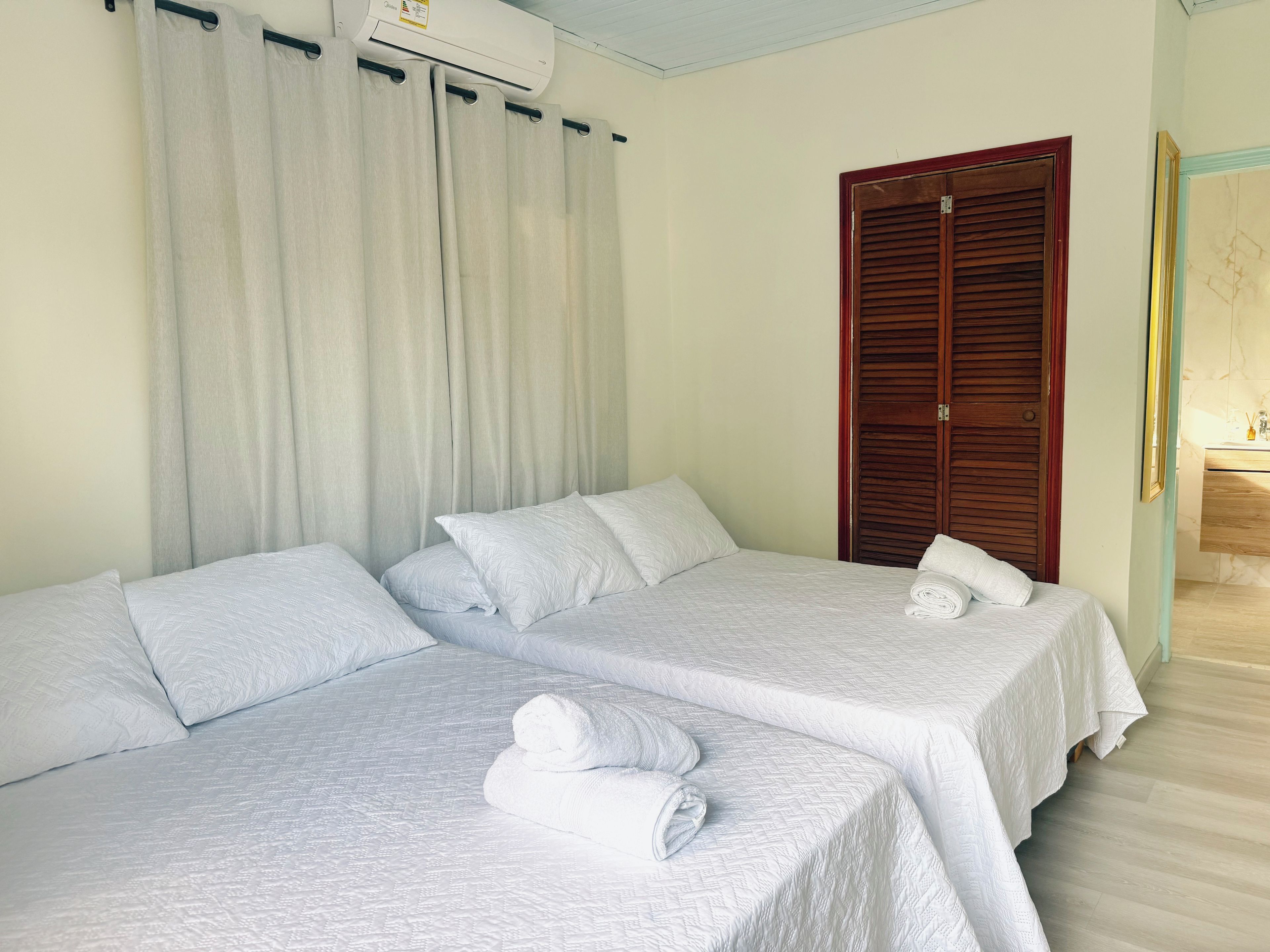 Habitación de hotel con dos camas, un armario de madera y un baño visible a través de una puerta abierta.