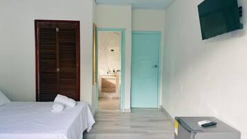 A bedroom with a bed, a wardrobe, a bathroom visible through an open door, and a TV mounted on the wall.